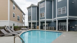 A swimming pool with lounge chairs and a wooden fence. - 4 BR Corner Unit Oceanfront Steps to it all! (Kure Beach)