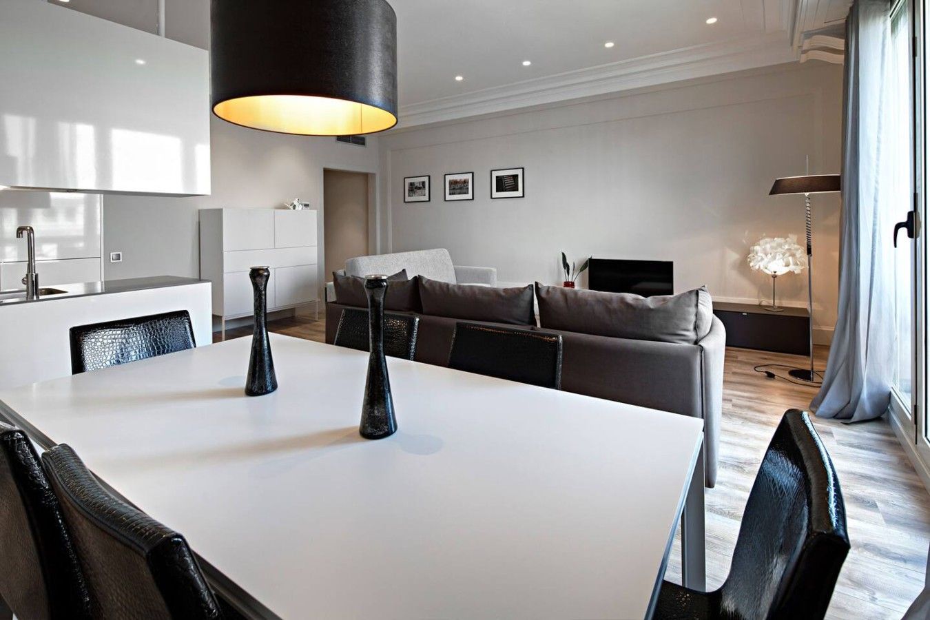 A modern living room with a white dining table, black chairs, a sofa, and a large black lamp.