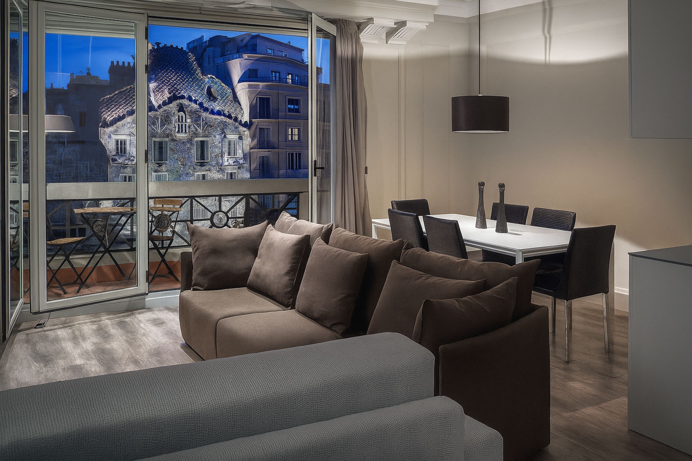 A modern living room with a sofa, a dining table with chairs, and a view of a historic building through large glass doors.