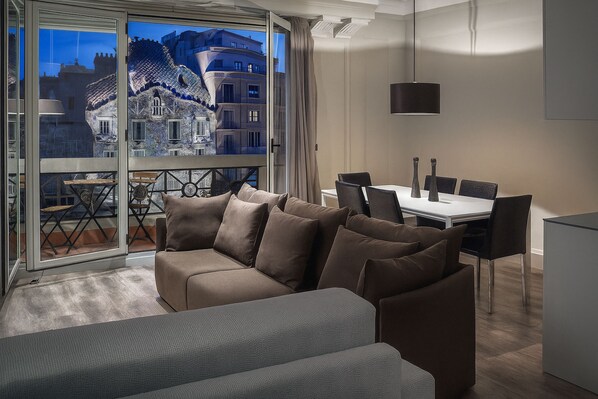 Un salon moderne comprenant un canapé, une table à manger avec des chaises, et offrant une vue sur un bâtiment historique grâce à de grandes portes vitrées.