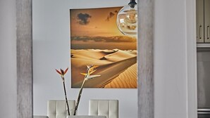 Une cuisine moderne agrémentée d’un grand tableau représentant un paysage désertique, d’un vase rempli de fleurs et d’un luminaire suspendu.