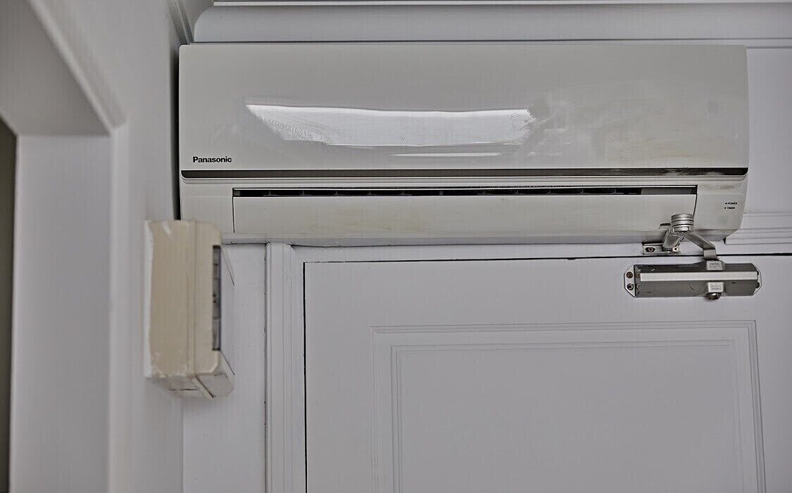 Un equipo de aire acondicionado Panasonic montado en una pared blanca junto a una puerta.
