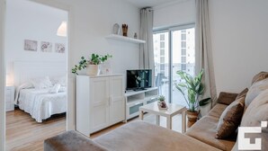 A modern living room with a sofa, a TV, a small table, and a bed with a white headboard. - El Mirador de Calpe 2E - Grupo Turis - Calpe, Costa Blanca (Calpe)