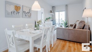 A modern living room with a grey sofa, a dining table set for four, and a large window providing natural light. - El Mirador de Calpe 2E - Grupo Turis - Calpe, Costa Blanca (Calpe)