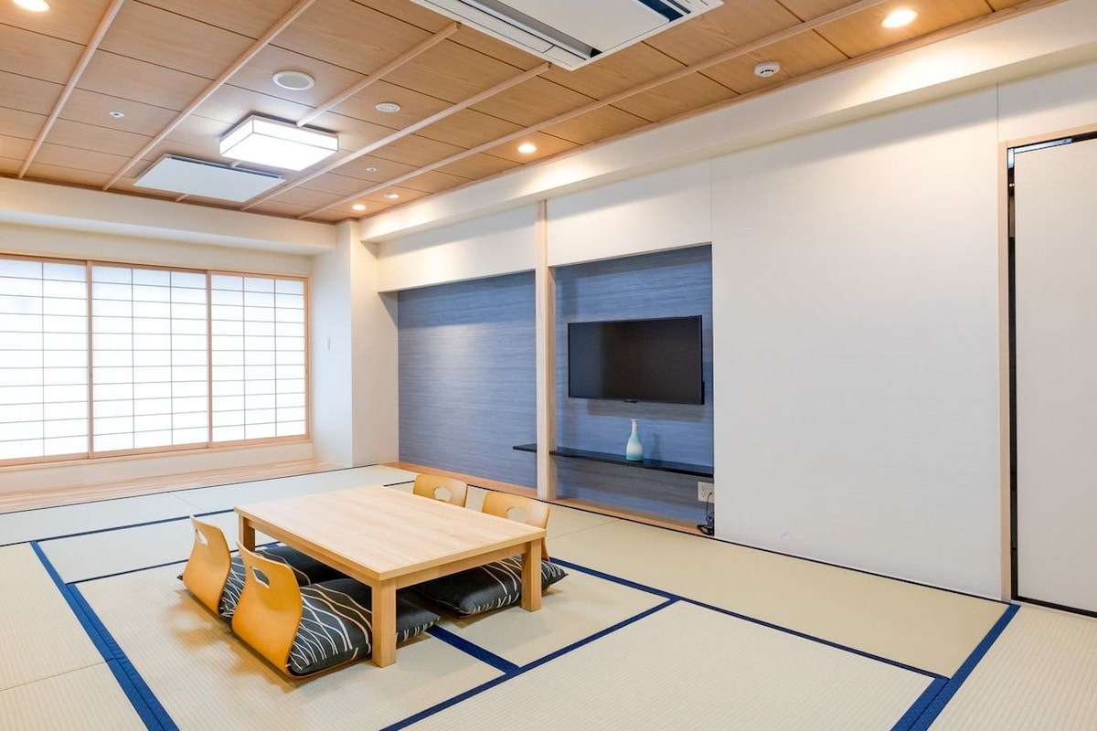 A room with tatami flooring, a wooden table, and a television on a shelf.
