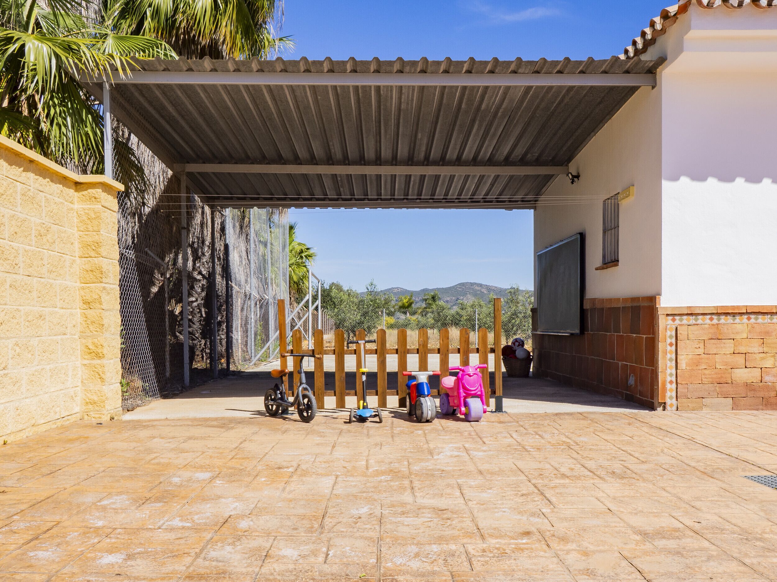 A covered outdoor area with a patio, a wooden fence, and a view of mountains in the background.