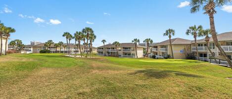 A hotel with multiple-story buildings, a grassy lawn, and palm trees.