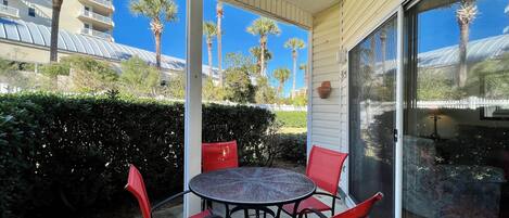 A covered outdoor patio with a round table and four red chairs, overlooking a residential area with palm trees and a white fence.