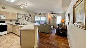 A spacious kitchen with a central island, wooden flooring, and a dining area with a table and chairs. - 1BR Beachwalk Condo | Easy Beach Access (Destin)