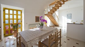 Un comedor con una mesa preparada para cuatro personas, una escalera de madera y una puerta amarilla con ventanas.