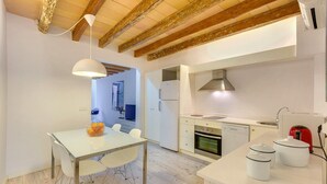 Une cuisine moderne avec des meubles blancs, un four encastré et une bouilloire rouge.