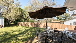 A backyard patio with a table and chairs, a large umbrella, and a wooden fence.