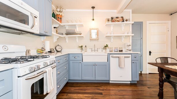 A kitchen with blue cabinets, a white stove, and wooden flooring.