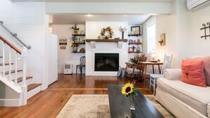 A living room with a fireplace, wooden floors, a sofa, a coffee table with a sunflower, and a staircase.
