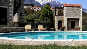 Ein Poolbereich mit Steingebäuden, einem Berg im Hintergrund und blauem Himmel.