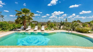 Ein klarer, blauer Himmel über Pool, Liegestühlen und einer Palme.
