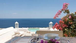 Une terrasse avec vue sur la mer, des meubles blancs et une table dressée pour le dîner.