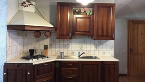 A kitchen with wooden cabinets, a gas stove, a sink, and a ceiling light. - House in the woods Osiglia, Liguria (Osiglia)