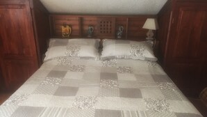 A bed with a checkered quilt, wooden headboard with decorative panels, and a bedside lamp. - House in the woods Osiglia, Liguria (Osiglia)
