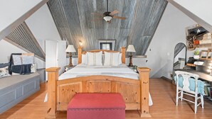 Un dormitorio con techo inclinado, cama de madera, un banco rojo y un escritorio con silla.