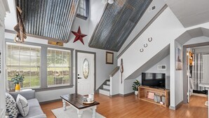 Una sala de estar moderna con una mesa de centro de madera, un sofá gris y un televisor. Hay una escalera que lleva a un nivel superior, y una decoración en forma de estrella roja en la pared.