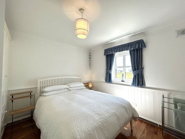 A bedroom with a bed, a bedside table, a window with curtains, a radiator, and a hanging light fixture.