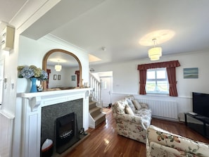 A living room with a fireplace, a sofa, a television, and a staircase leading to another room.