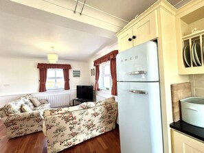 A compact living space with a sofa, a television, a white refrigerator, and a kitchen area with cabinets.