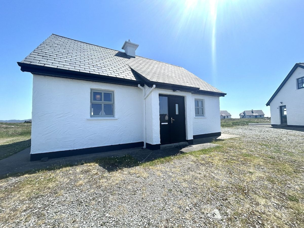 A single-story house with a dark roof and white walls, a front door, and a small window on the side.