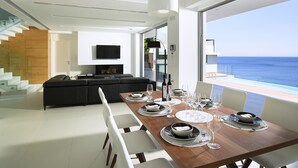 A modern dining area with a wooden table set for a meal, a black sofa, and a TV mounted on the wall.