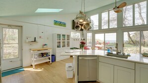 Een keuken met witte kastjes, een vaatwasser, een raam met uitzicht en een plafondventilator.