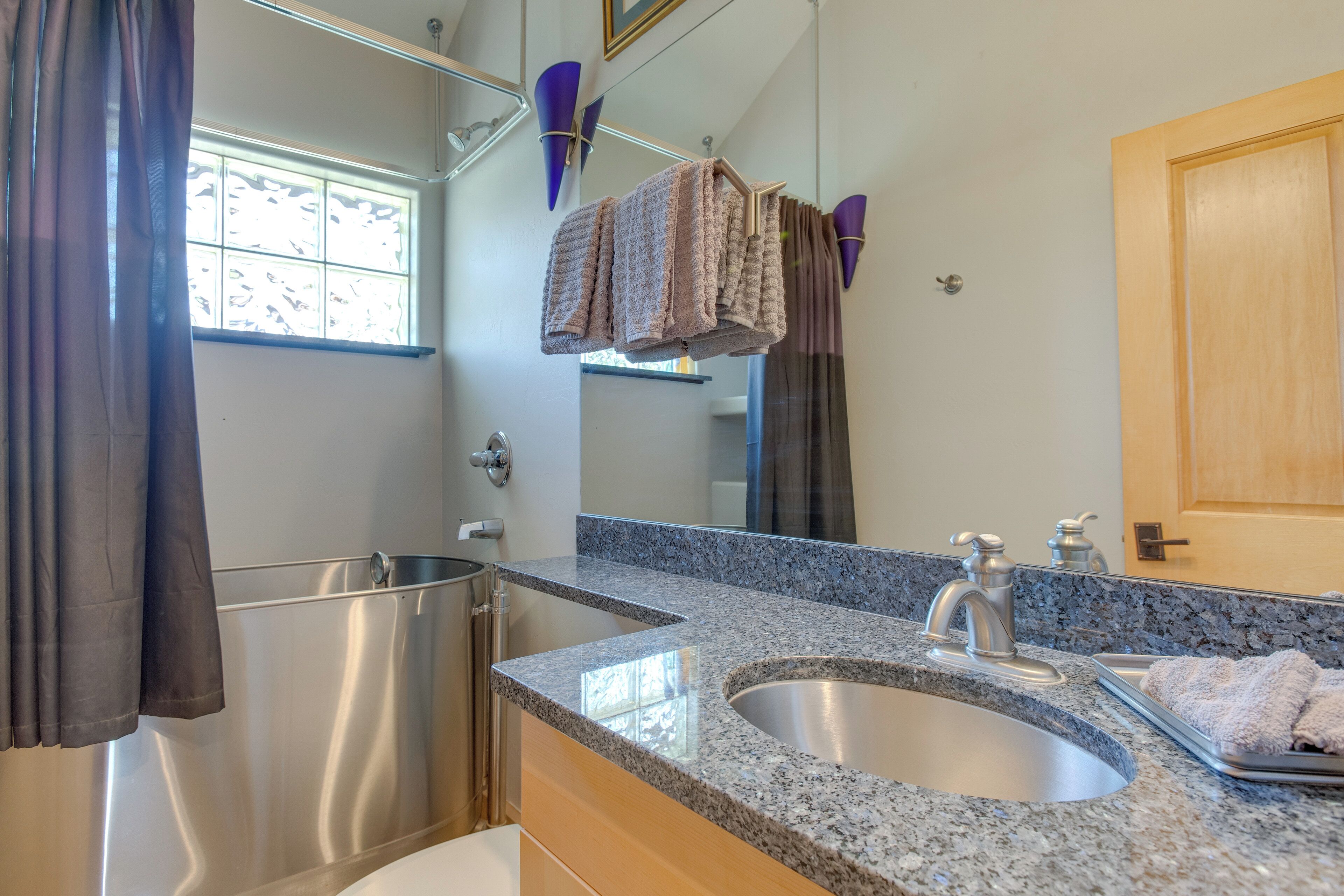 A bathroom with a granite countertop, a sink, a mirror, and towels hanging on a rack.