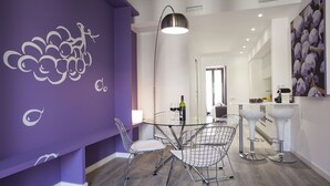 Un comedor moderno con una pared de acento morada, una mesa de vidrio, sillas de metal y una lámpara colgante.