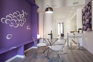 A modern dining area with a purple accent wall, a round glass table, and metal wire chairs.