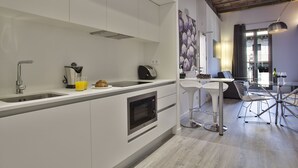 Una cocina moderna con armarios blancos, horno integrado y comedor con mesa de vidrio y sillas de metal.