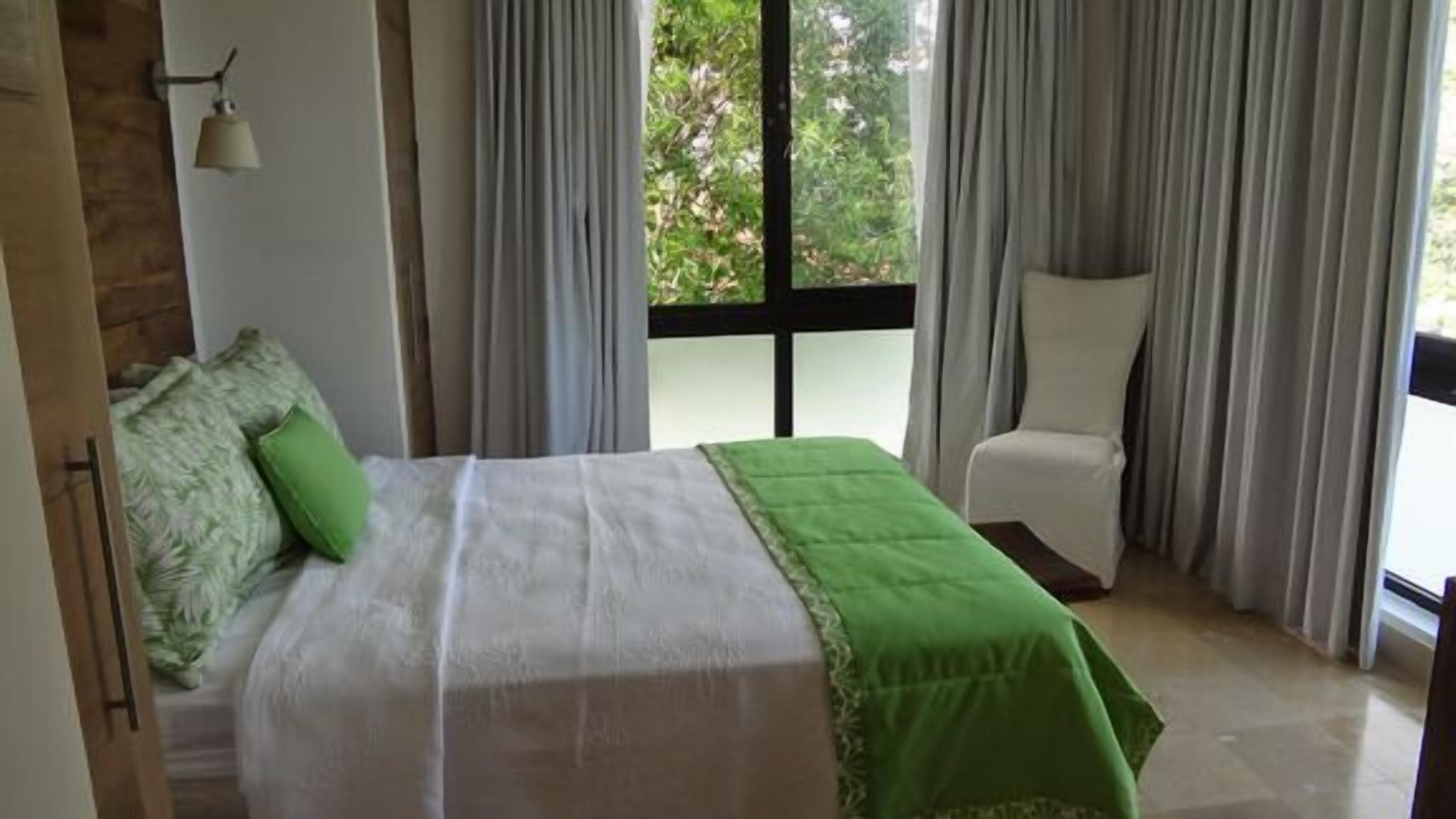 Een slaapkamer met een bed, een stoel en een raam met gordijnen.