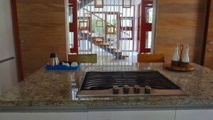 Eine Küche mit einem Gasherd, einer blauen Serviertablett mit Küchenutensilien und Blick auf eine Treppe sowie einen Außenbereich durch eine Glastür.
