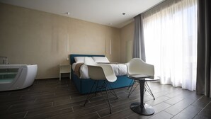 A modern hotel room with a bed, a seating area, a small table, and a bathtub. - Quaint Boutique Hotel Sannat (Sannat)