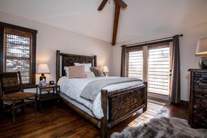 A bedroom with a wooden bed, two bedside tables, a chair, and a large window with blinds. - Beautiful Home on Home Again Trail 3BR ski in-out. 5 star home, 5 star location (Whitefish)