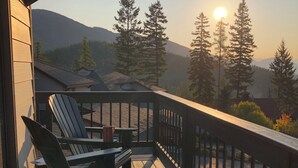 Une terrasse en bois, agrémentée de chaises Adirondack et d’une table, offrant une vue sur un paysage montagneux, avec des arbres et un ciel dégagé.