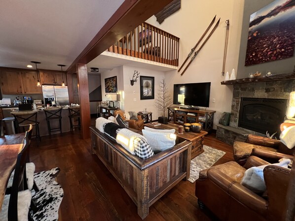 A spacious living area with a high ceiling, a fireplace, a television, and a dining area with a kitchen in the background. - Beautiful Home on Home Again Trail 3BR ski in-out. 5 star home, 5 star location (Whitefish)