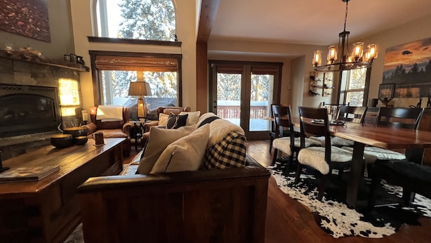 Un salon chaleureux avec une cheminée, une grande fenêtre et un coin repas doté de meubles en bois.