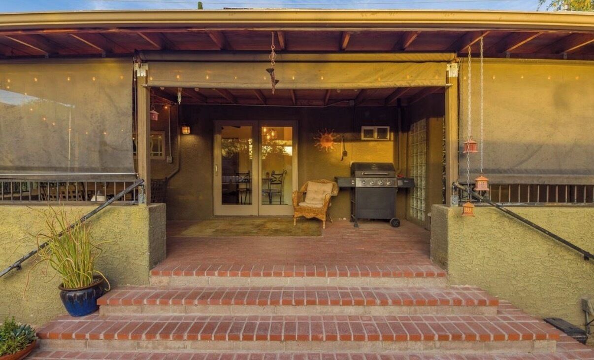 A covered patio with steps leading to a door, a grill, and a chair.