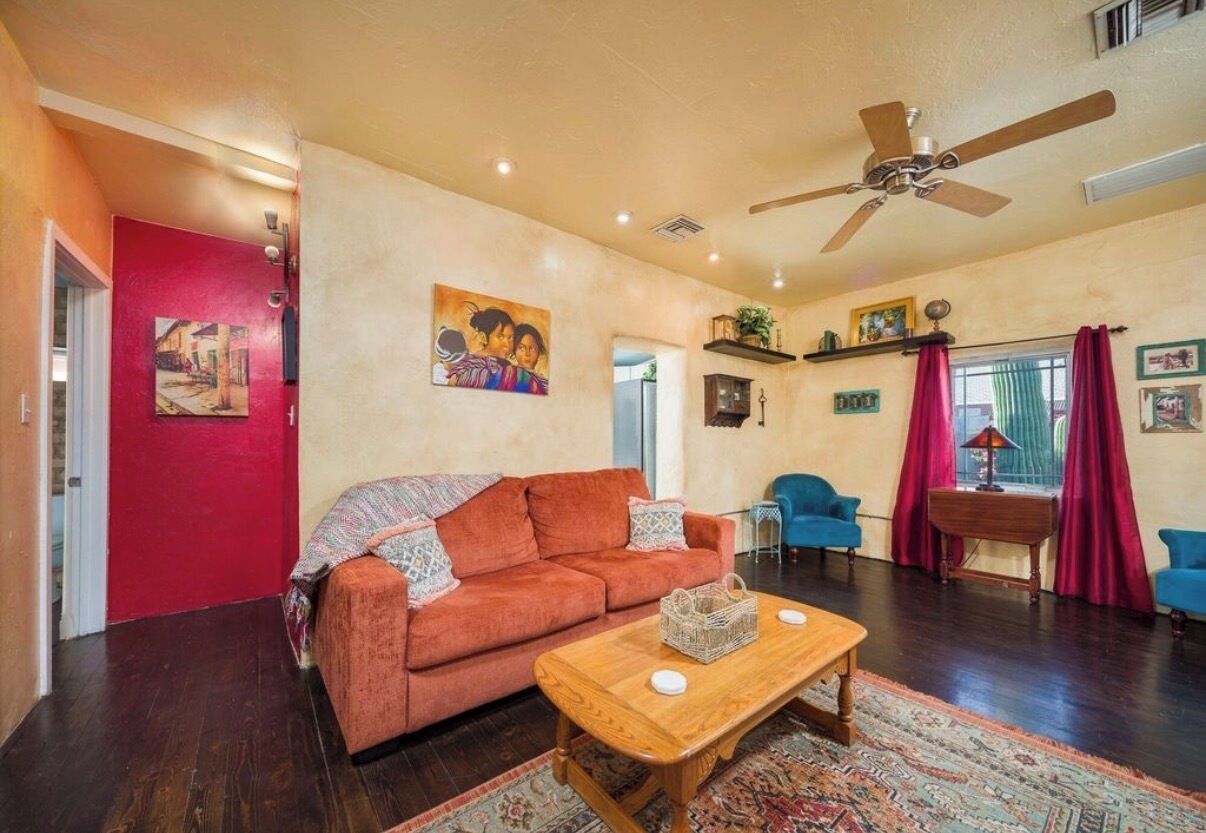 A living room with a sofa, a coffee table, a ceiling fan, and a red door.