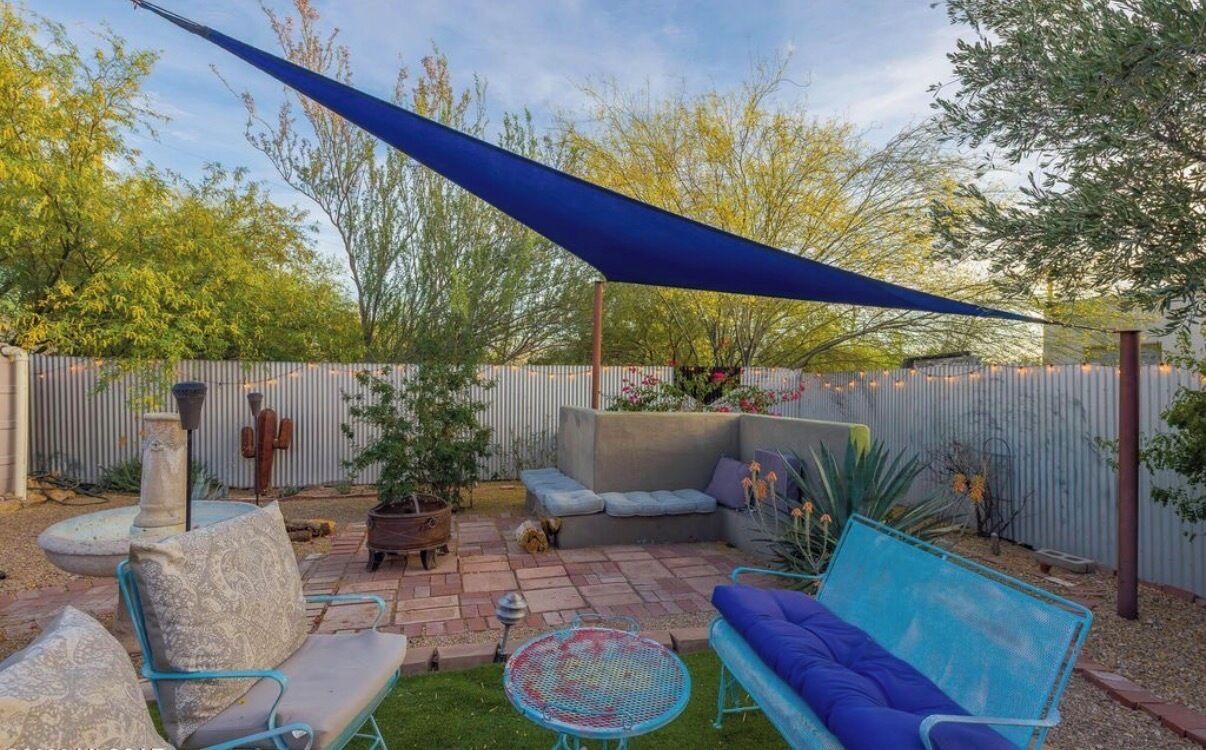A patio with a blue canopy, seating, a small table, and potted plants.
