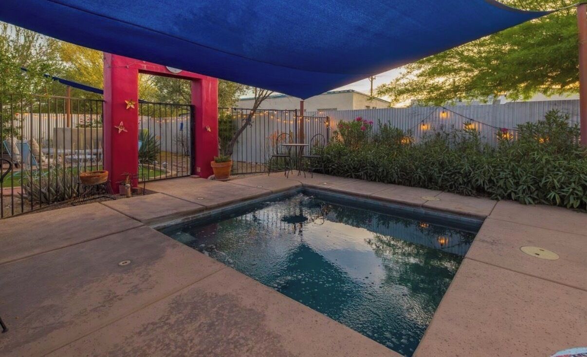 A swimming pool area with a red gate, a blue canopy, and a fence with string lights.