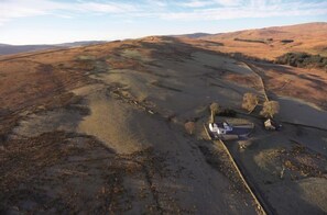 A rural landscape with rolling hills and a small building with a car parked outside.