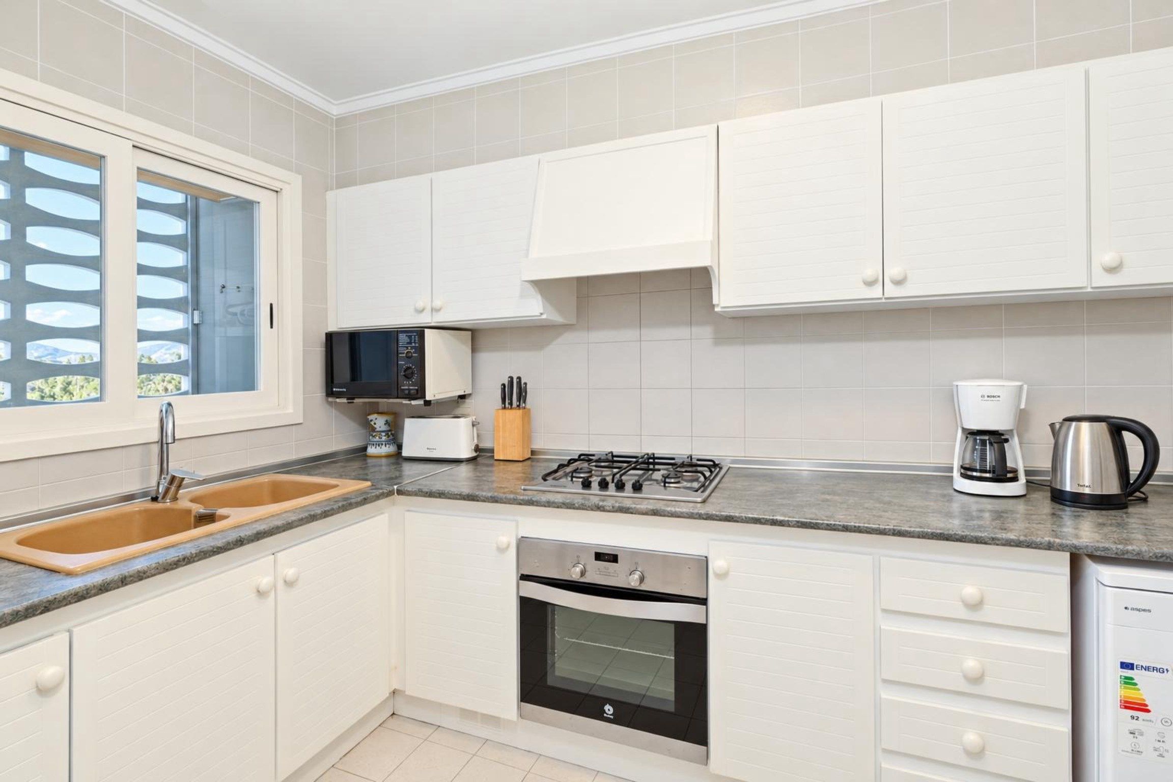 Een moderne keuken met witte kasten, een roestvrijstalen fornuis, een inbouwoven, een magnetron en een koffiezetapparaat.