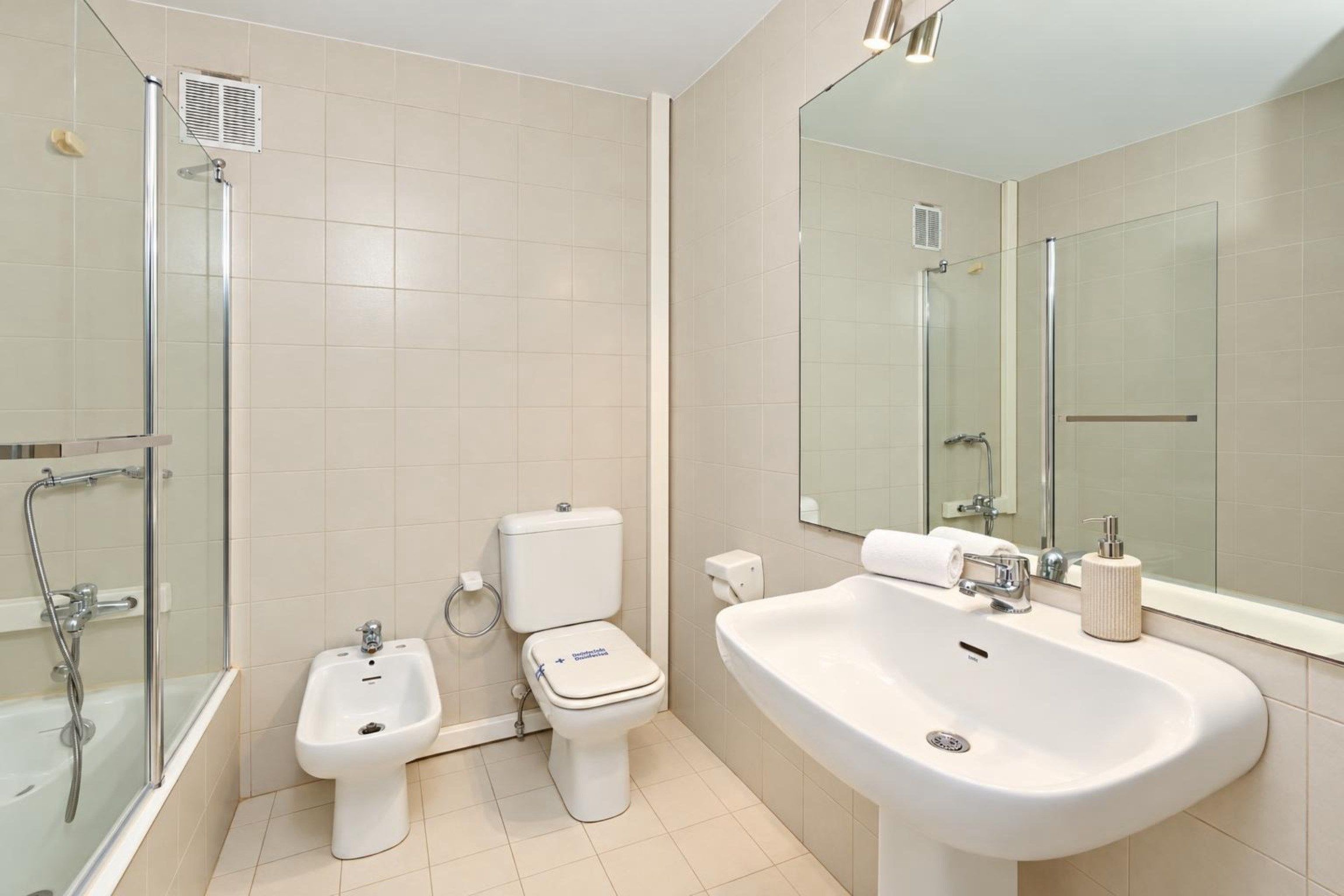 Une salle de bain moderne équipée d’une douche, d’un bidet, de toilettes, d’un lavabo et d’un grand miroir.