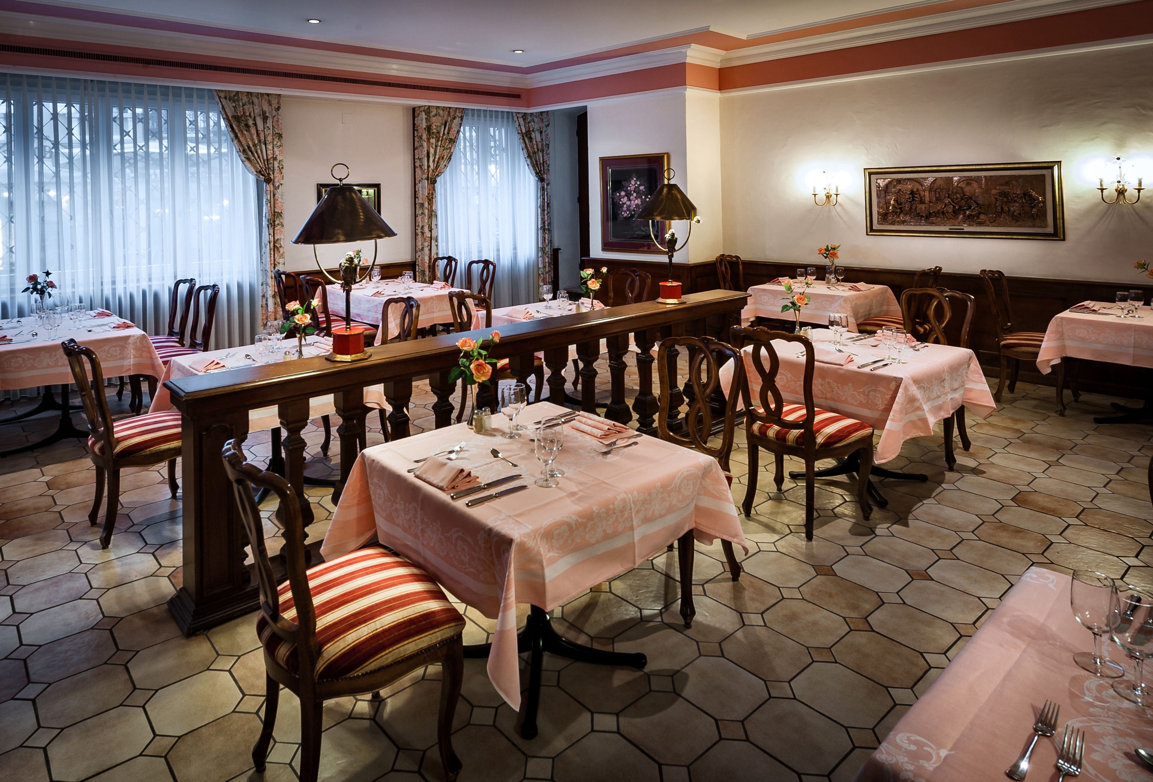 A dining area with hexagonal tiled flooring, wooden chairs with striped cushions, and tables set with white tablecloths and silverware.
